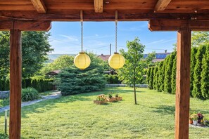 A wooden pergola with two hanging lanterns, surrounded by a well-maintained garden with a pathway, potted plants, and a view of a residential area. - Pool House Green View /w Jacuzzi & Garden (Oroslavje)