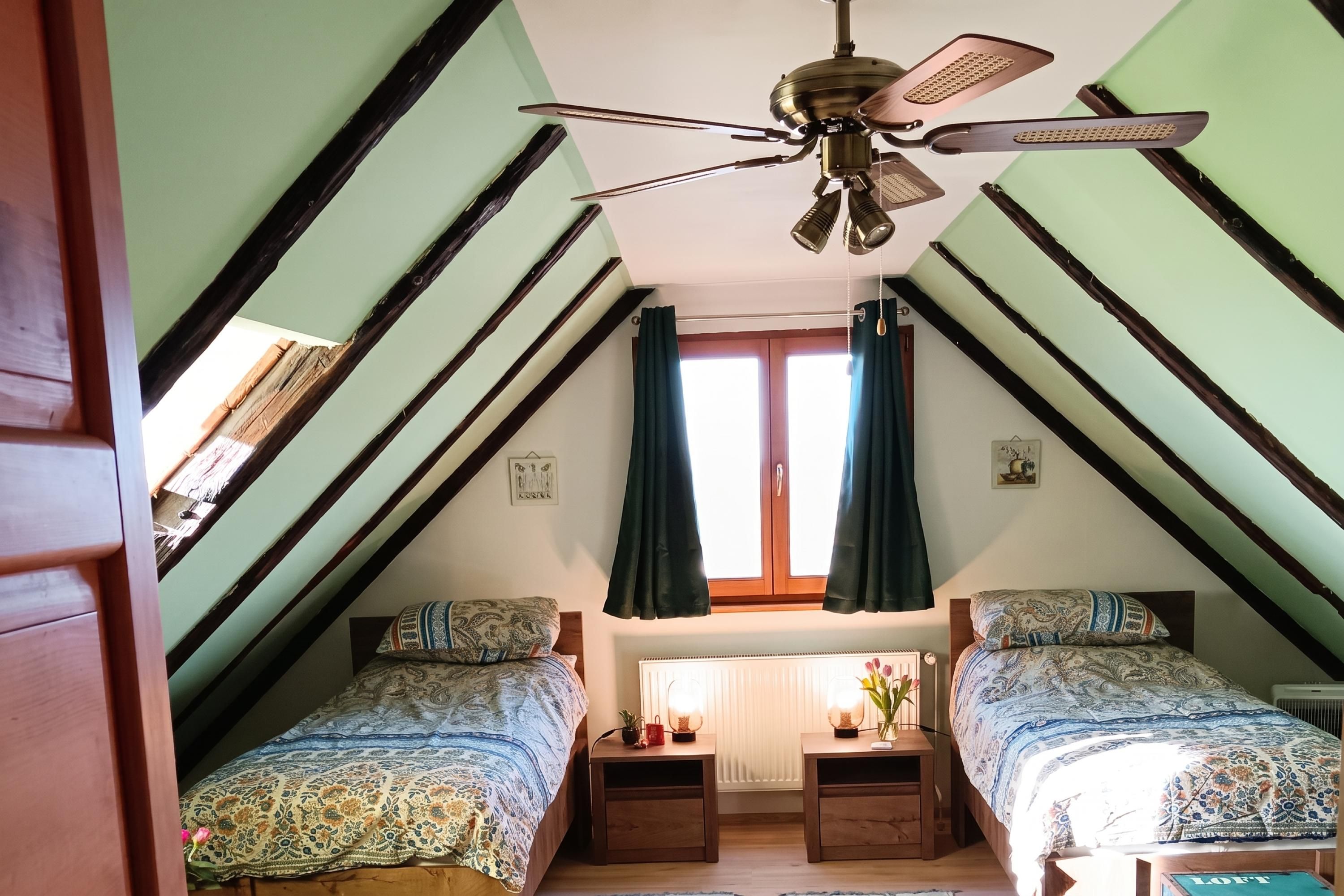 Un dormitorio con techo inclinado, dos camas, una ventana con cortinas y un ventilador de techo.