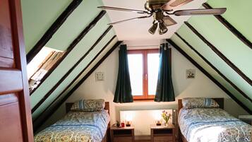 Un dormitorio con techo inclinado, dos camas, una ventana con cortinas y un ventilador de techo.