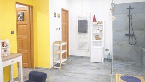 Casa de banho com chuveiro, sanita, lavatório e espelho. Tem uma prateleira com artigos de higiene e um porta-toalhas.
