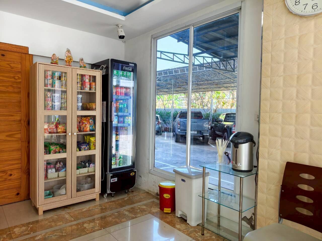 Una habitación con una máquina expendedora, un mueble de vidrio con aperitivos, una ventana que da a coches aparcados y un reloj en la pared.