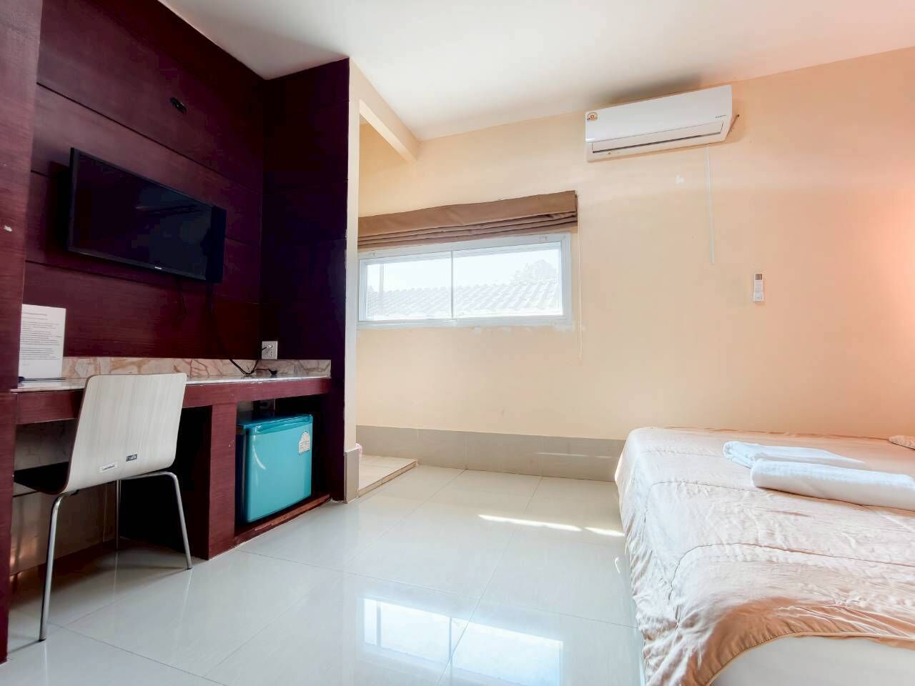 Quarto de hotel com cama, secretária com cadeira, pequeno frigorífico, televisão e janela com vista para o exterior.