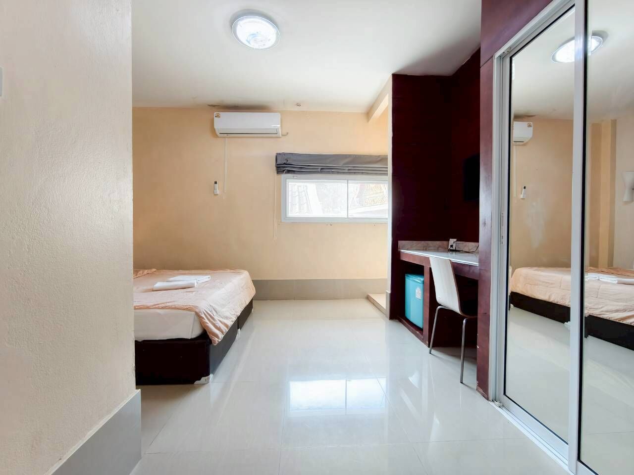 A compact room with two beds, a desk, and a large mirror.