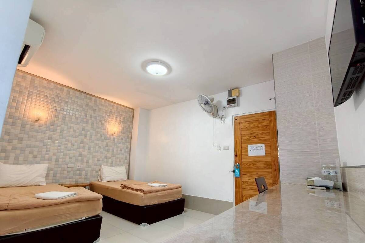 Une chambre d’hôtel avec deux lits, une porte en bois, un téléviseur à écran plat et un mur recouvert de carreaux.