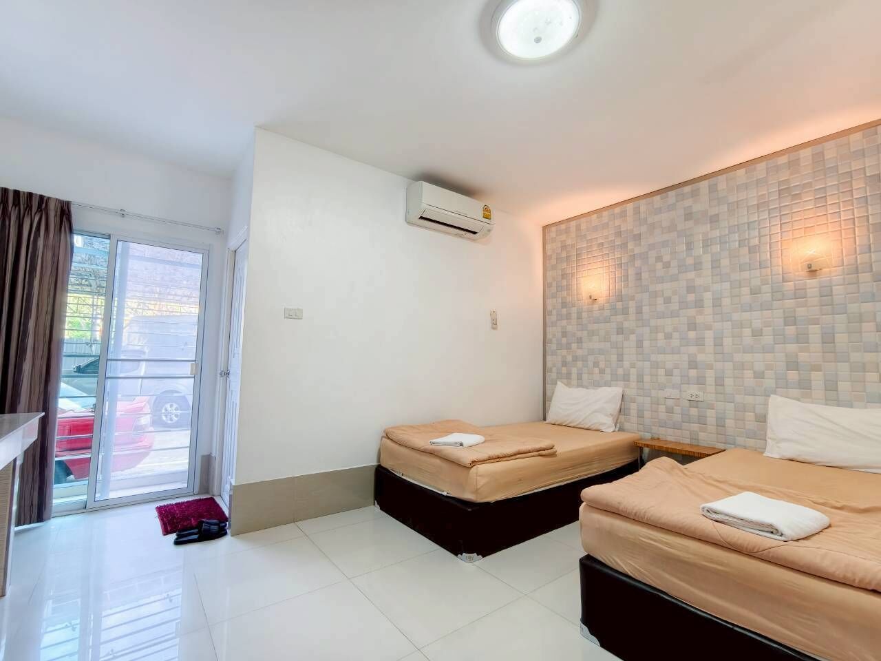 A hotel room with two beds, a sliding glass door to the outside, an air conditioning unit, and a tiled wall.