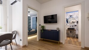 Un soggiorno moderno con una TV montata a parete, un tavolino consolle blu scuro con una pianta e un pavimento in legno.