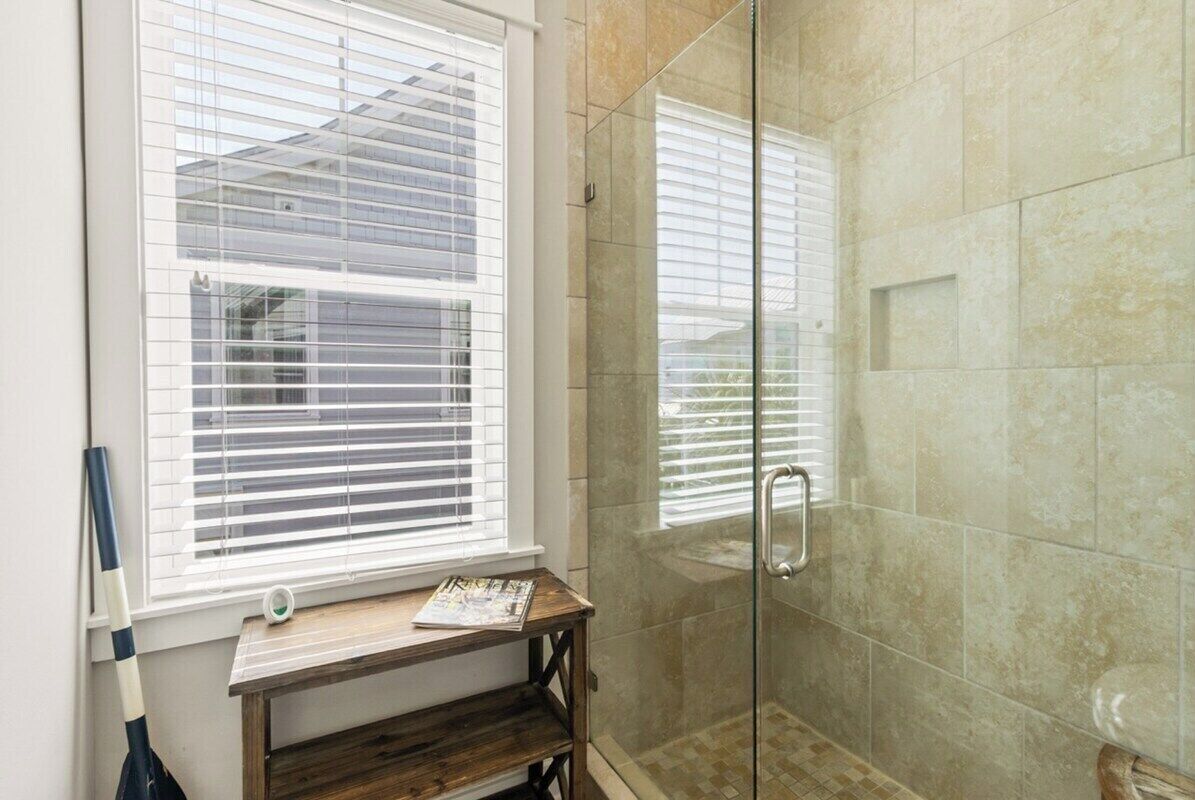 Un baño con mampara de vidrio, una ventana con persianas y un estante de madera.