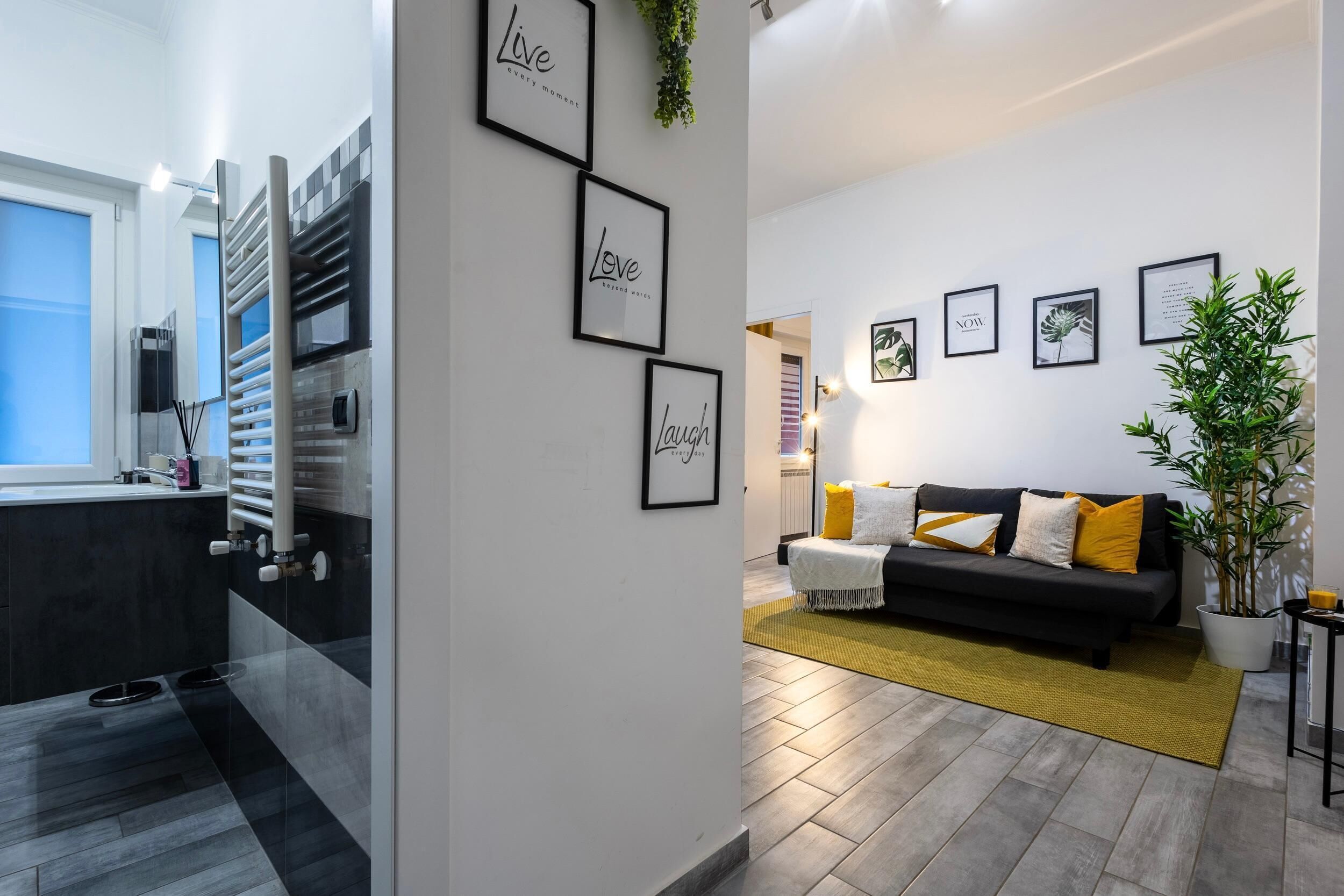 Ein modernes Wohnzimmer mit einem schwarzen Sofa, gelben Kissen und einer Topfpflanze.