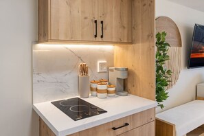 A modern kitchen with wooden cabinets, a marble backsplash, a built-in induction cooktop, and a coffee machine. - Waikiki Luxe Haven – Chic Comfort in Paradise (Honolulu)