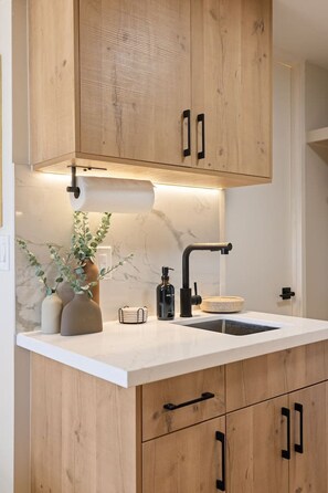 A modern kitchen with wooden cabinets, a white countertop, a black faucet, and a marble backsplash. - Waikiki Luxe Haven – Chic Comfort in Paradise (Honolulu)
