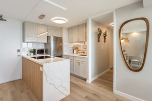 Una cocina moderna con armarios blancos, una isla de mármol y un espejo grande.