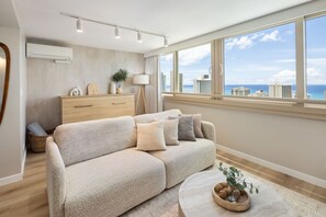 Una sala de estar moderna con un sofá color beige, una mesita de madera y vistas de la silueta urbana a través de amplias ventanas.