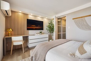 Un dormitorio moderno con una cama, un escritorio, una silla, un televisor y una planta.