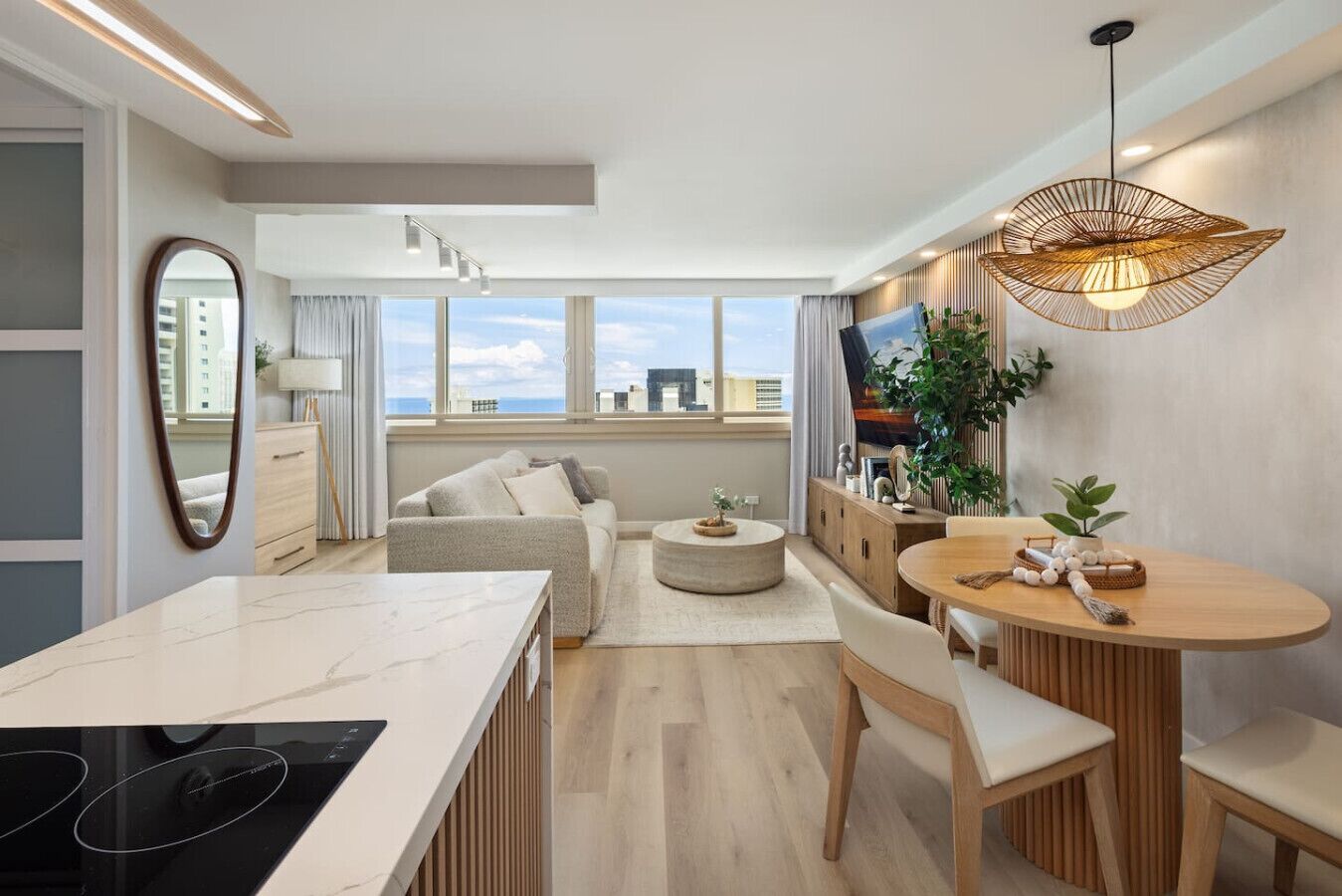 A modern apartment with a kitchen, dining area, and living room. It features large windows, a flat-screen TV, and a unique pendant light. - Waikiki Ocean Luxe Retreat High Floor Suite (Honolulu)