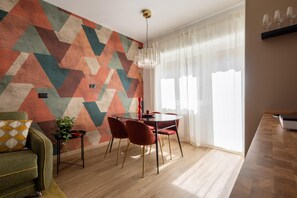 Een eetruimte met een wand met een geometrisch patroon, een ronde tafel met stoelen en een kroonluchter.