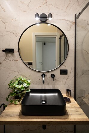 Een badkamer met een ronde spiegel, een zwarte wastafel, een plant in pot en een marmeren wand.