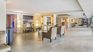 Een ruime hotellobby met een hoge plafond, een receptiebalie, zithoeken en een groot schilderij aan de muur.