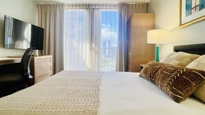 Een hotelkamer met een groot bed, een bureau met stoel, een televisie en een raam met gordijnen.