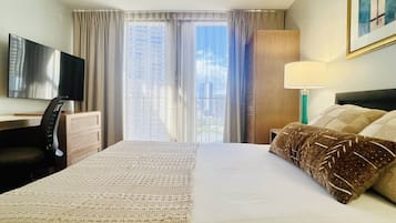 Une chambre d’hôtel avec un grand lit, un bureau avec une chaise, une télévision et une fenêtre avec des rideaux.
