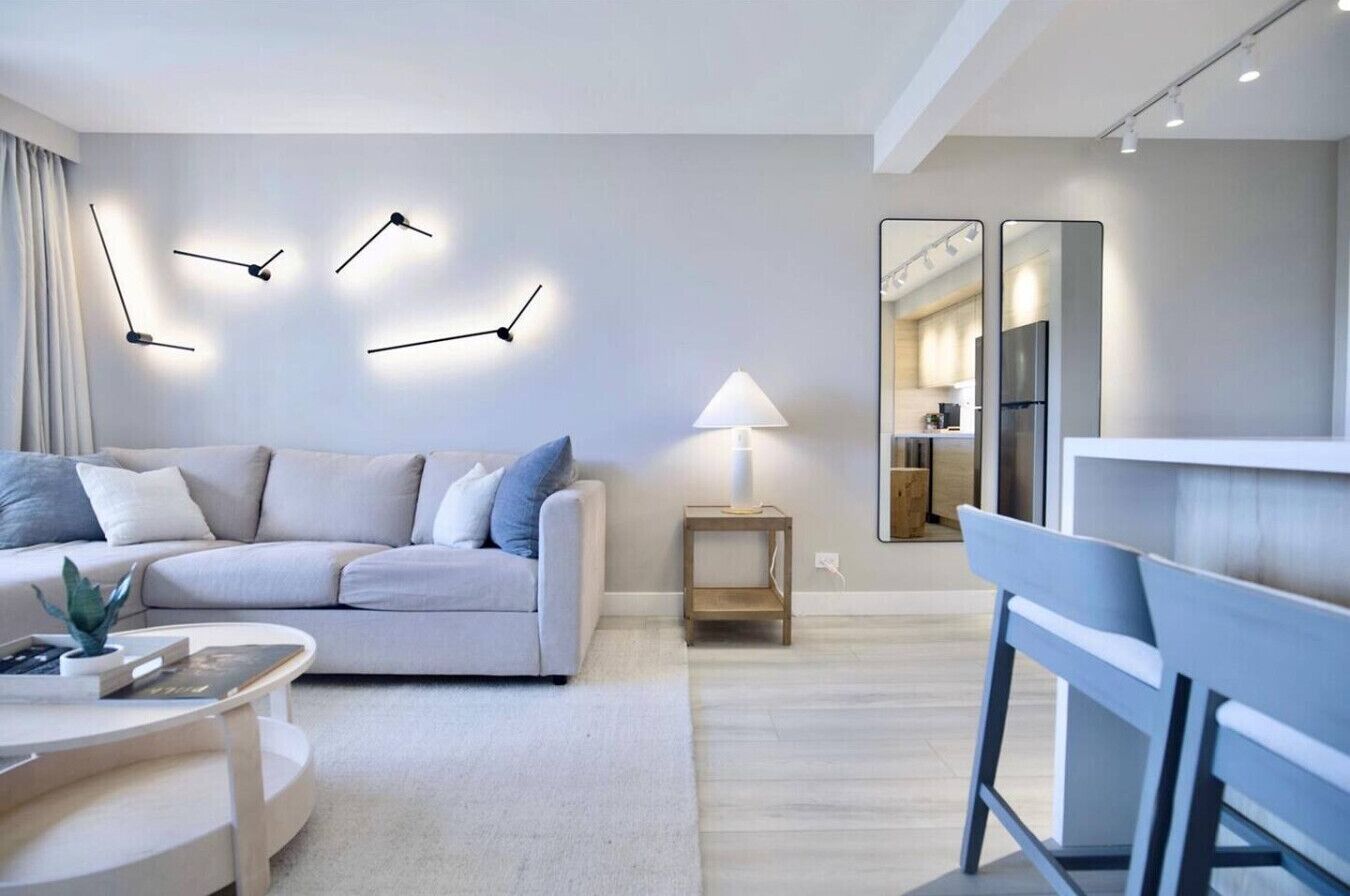 Een moderne woonkamer met een bank, een salontafel, een bijzettafeltje met een lamp, en een eethoek met een stoel en een spiegel.