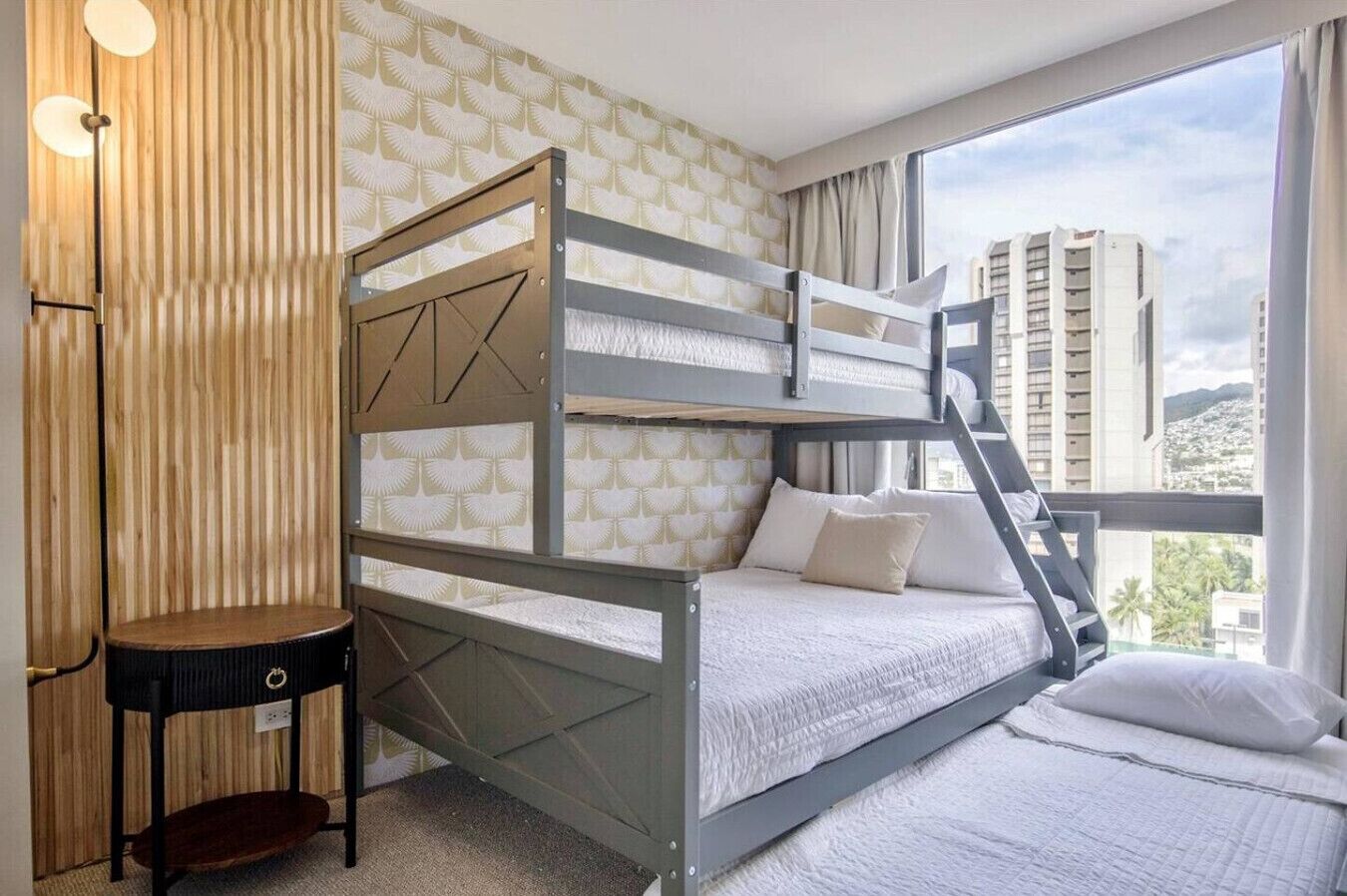 A bunk bed room with a view of buildings through large windows.