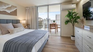 Ein Schlafzimmer mit Bett, Nachttisch, Lampe, großem Fenster und einem Balkon mit Tisch und Stühlen.
