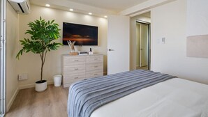 Ein Schlafzimmer mit Bett, einem Schminktisch, einer Topfpflanze und einem Bild an der Wand.