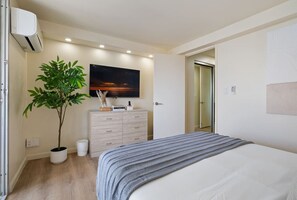 Un dormitorio con cama, cómoda, planta en maceta y un cuadro en la pared.