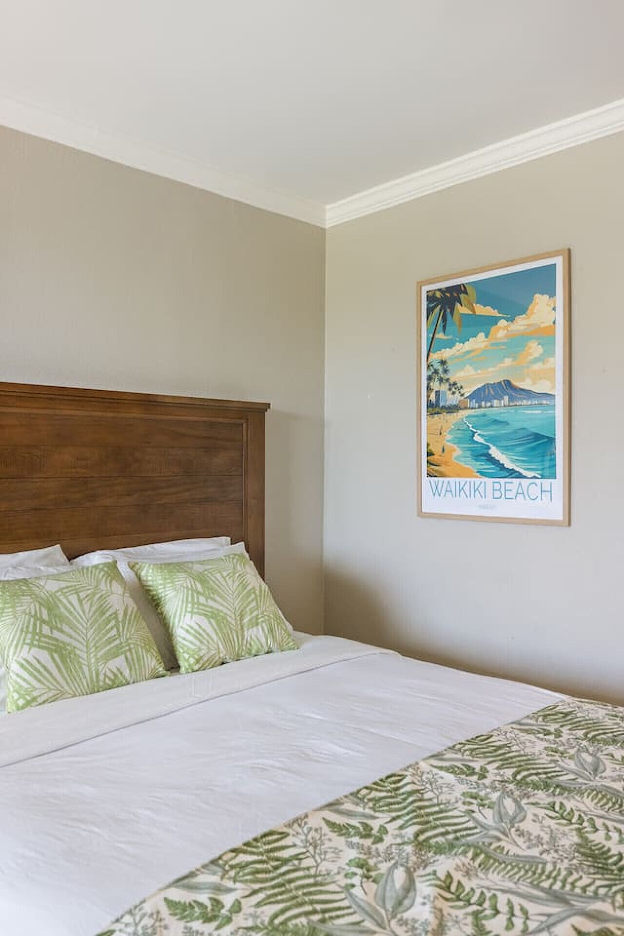 A bed with a wooden headboard, a green patterned bedspread, and a framed picture of Waikiki Beach on the wall.