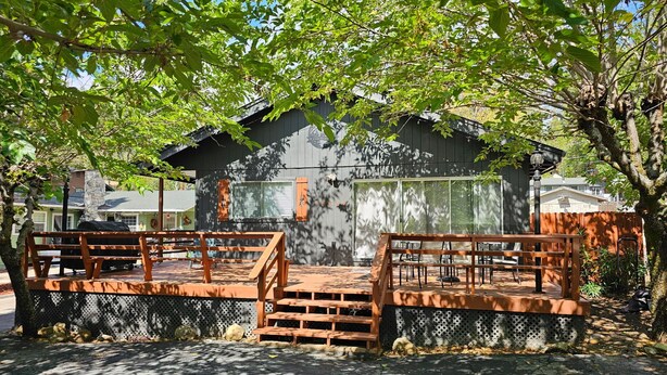 A wooden deck with benches, a grill, and a building with a large window and a clock. - Hot Tub, Walk to Town, Lake Access, Fireplace, Fenced Yard (Twain Harte)