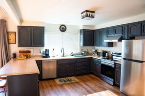A modern kitchen with dark cabinetry, stainless steel appliances, and a wooden countertop.