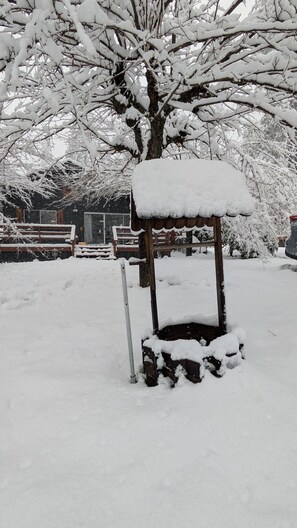 A snow-covered outdoor structure with a roof, surrounded by snow-laden trees and a fence in the background.