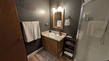 Een badkamer met een houten wastafelmeubel, een wastafel, een spiegel met verlichting, een handdoekhouder en een douchehoek.