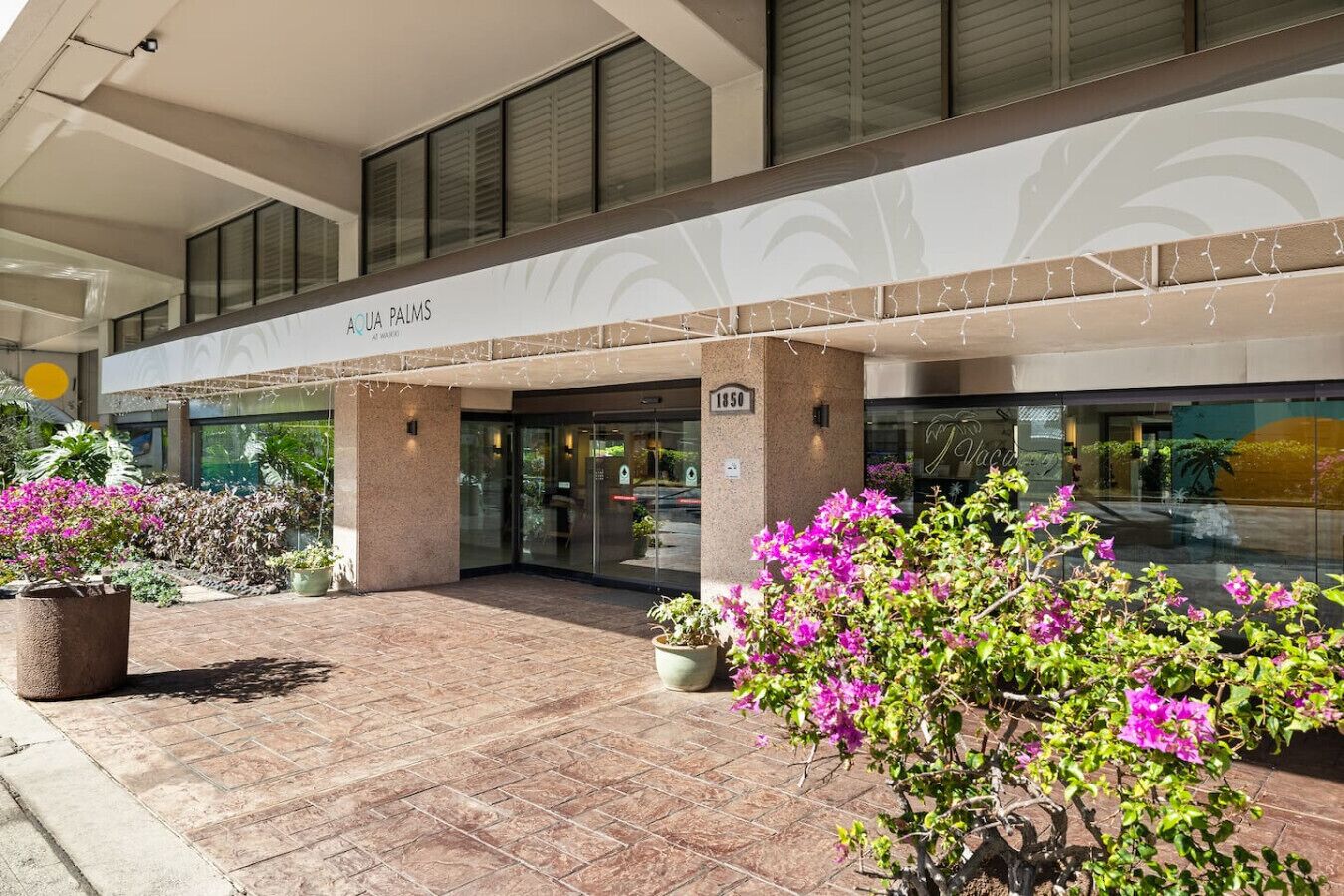 A hotel entrance with a covered walkway, glass doors, and potted plants.