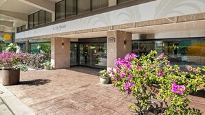Ein Hotel mit Eingangsbereich, überdachtem Gang, Glastüren und Pflanzen in Töpfen.