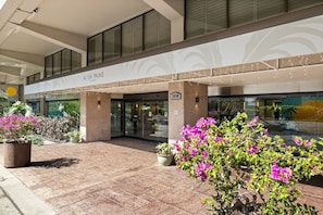 A hotel entrance with a covered walkway, glass doors, and potted plants. - Waikiki Ocean Breeze: A Peaceful Island Getaway (Honolulu)