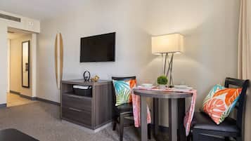 A hotel room with a flat-screen TV, a small table with chairs, a desk with drawers, and a bed.