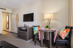 A hotel room with a flat-screen TV, a small table with chairs, a desk with drawers, and a bed. - Waikiki Ocean Breeze: A Peaceful Island Getaway (Honolulu)