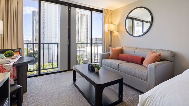 Ein modernes Hotelzimmer mit Balkon, einer Sitzecke, einem Couchtisch und einem Schreibtisch mit Lampe.