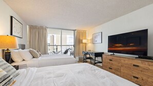 A hotel room with two beds, a desk, a television, and a view of the cityscape. - Heart of Waikiki • Steps to Beach • Cozy Studio (Honolulu)