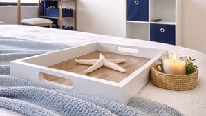 A neatly arranged bedroom with a bed, a starfish in a box, a TV, and a plant.