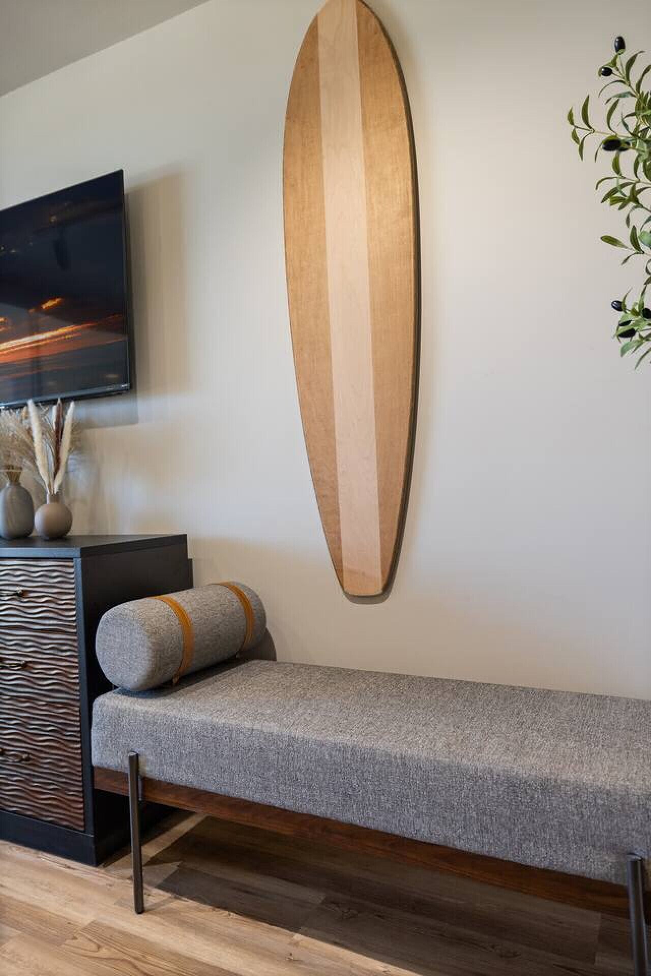 Un soggiorno moderno con un divano grigio, un'asse da surf in legno, una TV a schermo piatto e una pianta.