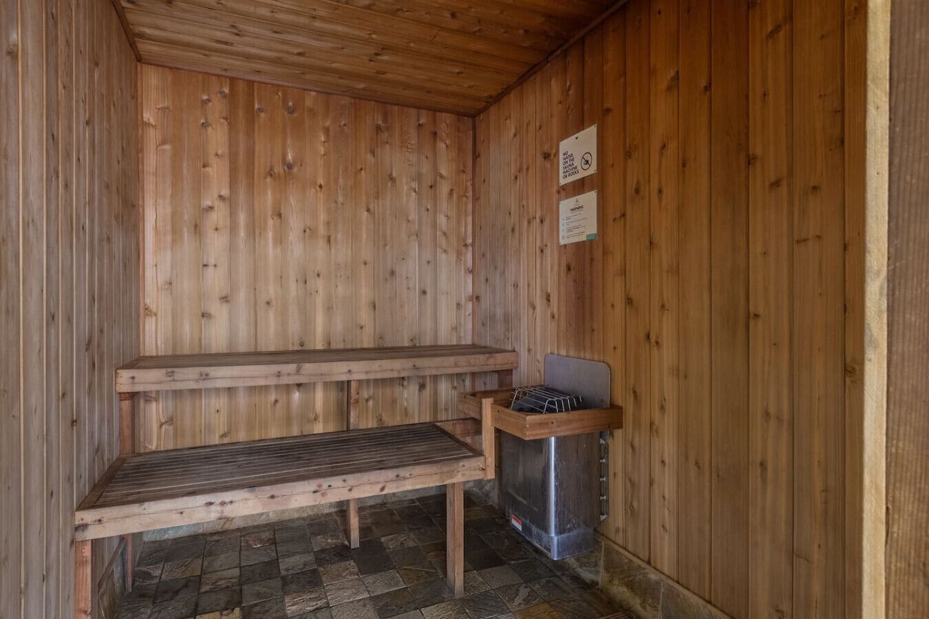 En träbeklädd bastu med sittbänkar och en metallkamin.