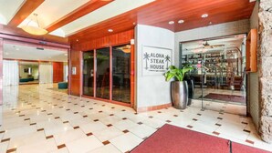 En hotellobby med ett rutmönstrat golv, en stor krukväxt och en skylt för Aloha Steak House.