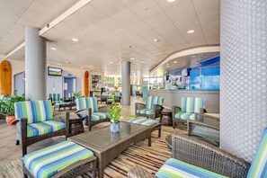 Eine geräumige Lobby mit Korbmöbeln und Streifenpolstern, ein Empfangsbereich mit Theke und eine große Säule.