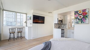 A modern hotel room with a bed, a small kitchenette, a dining area with two chairs, and a large window. - Corner Bliss in the Heart of Waikiki 8F (Honolulu)