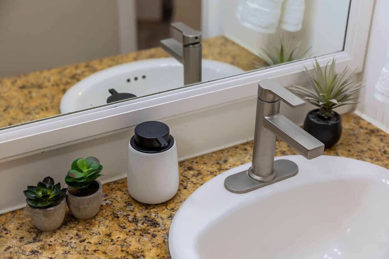 Un bagno con un piano di lavoro in granito, un lavandino bianco, uno specchio, un rubinetto e due piccole piante in vaso.