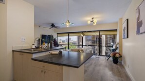 A modern kitchen with a large island, a ceiling fan, and a view through large windows. - Urban Paradise with a Complimentary Parking (Honolulu)