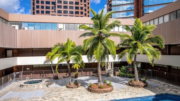 A pool area with palm trees, a hot tub, and a building in the background. - Urban Paradise with a Complimentary Parking (Honolulu)