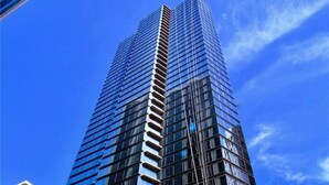 A high-rise building with a modern glass facade, a visible entrance with a sign, and a street in the foreground. - Urban Paradise with a Complimentary Parking (Honolulu)